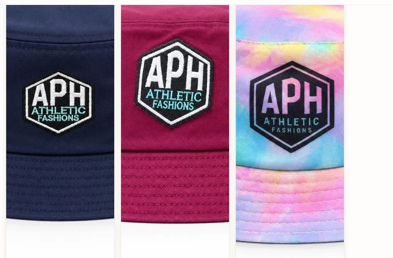 Close-up of the APH hexagon patch on three bucket hats: embroidered on navy and on magenta, printed on pastel tie-dye